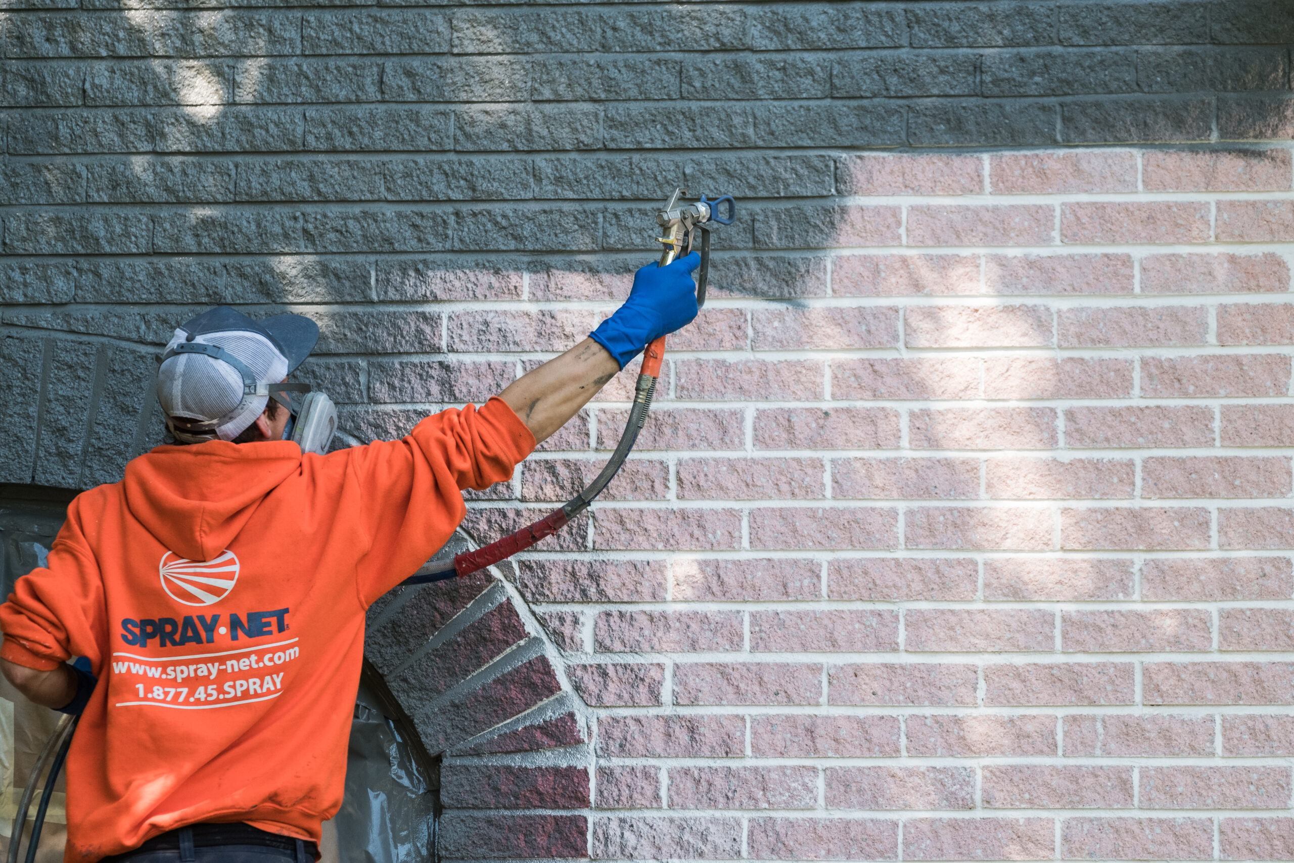 Spray-Net technician applying gray brick stain to an exterior brick wall