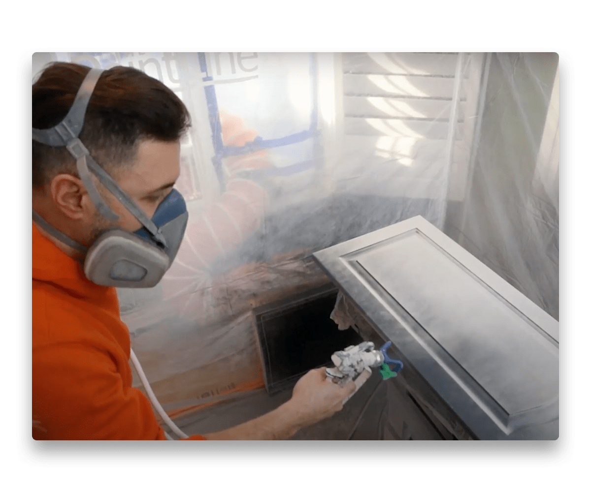 An image depicting a painter spray painting a kitchen cabinet door.